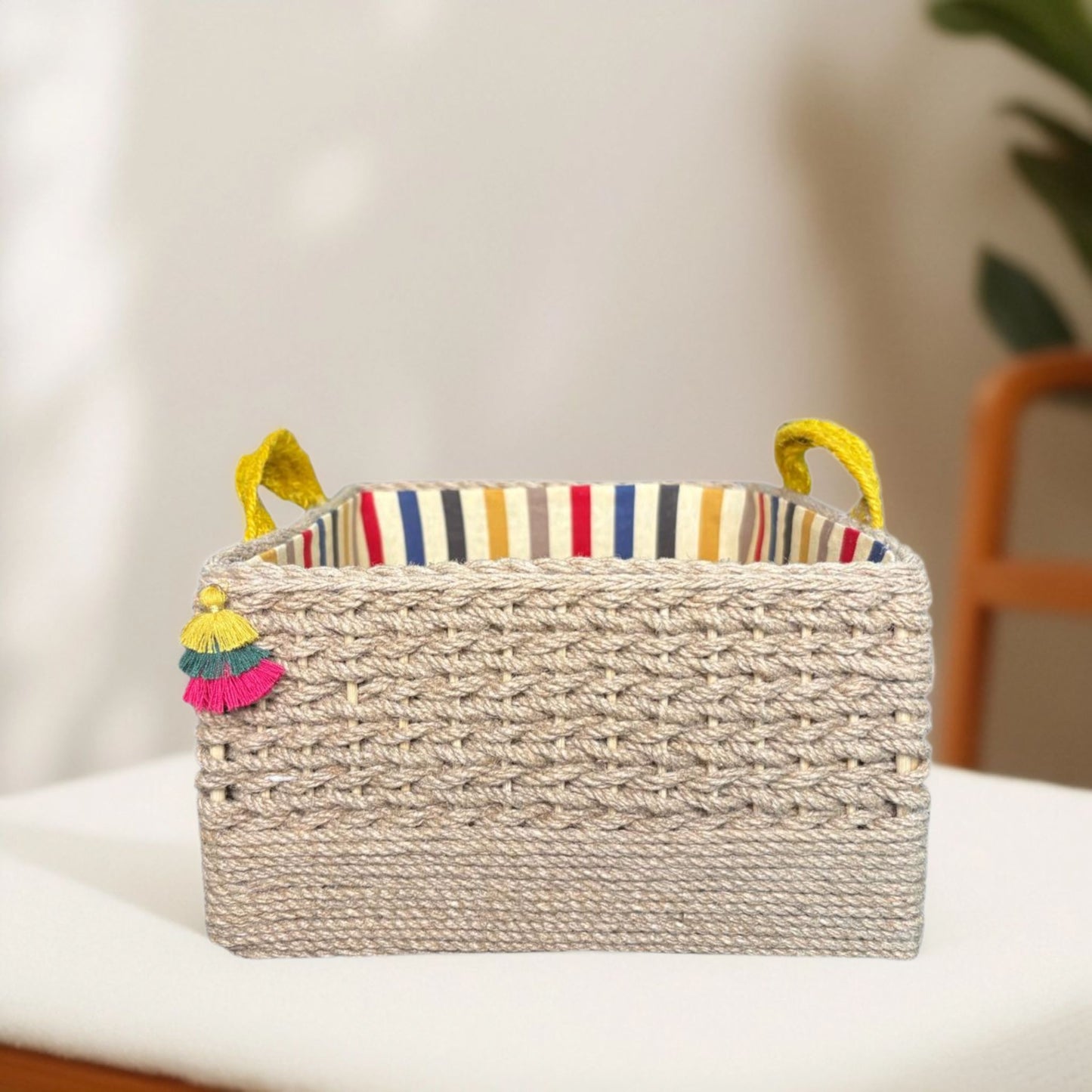 Woven storage basket with colorful striped interior and tassels on a white surface.